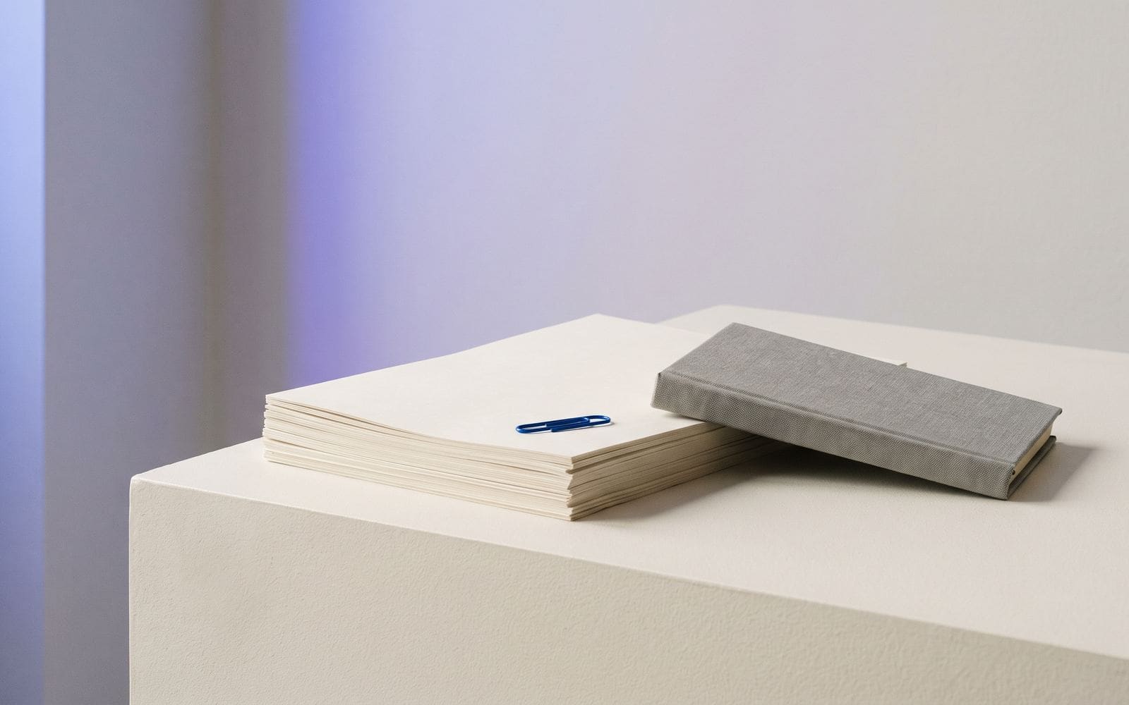 A stack of blank statements and a closed ledger book with a single blue paper clip