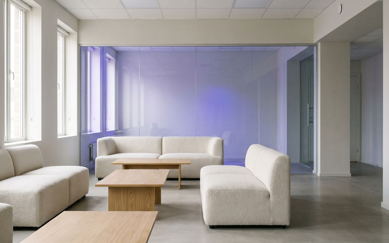 A coworking lounge with pale sofas, oak tables, and tall windows